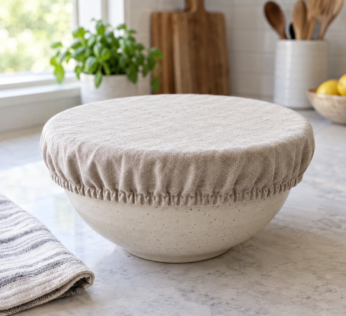 Saladier en céramique recouvert d'un couvre-plat en tissu lavable à bord élastiqué sur une table de cuisine.